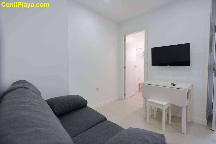 Salón con sofá gris, mesa blanca y televisión en la pared