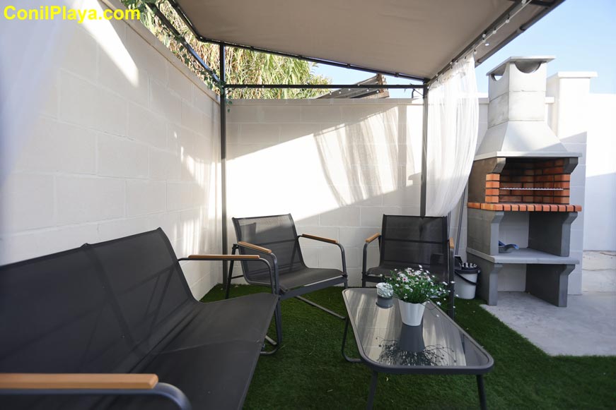 Zona exterior con sillones bajo pérgola y barbacoa junto a mesa