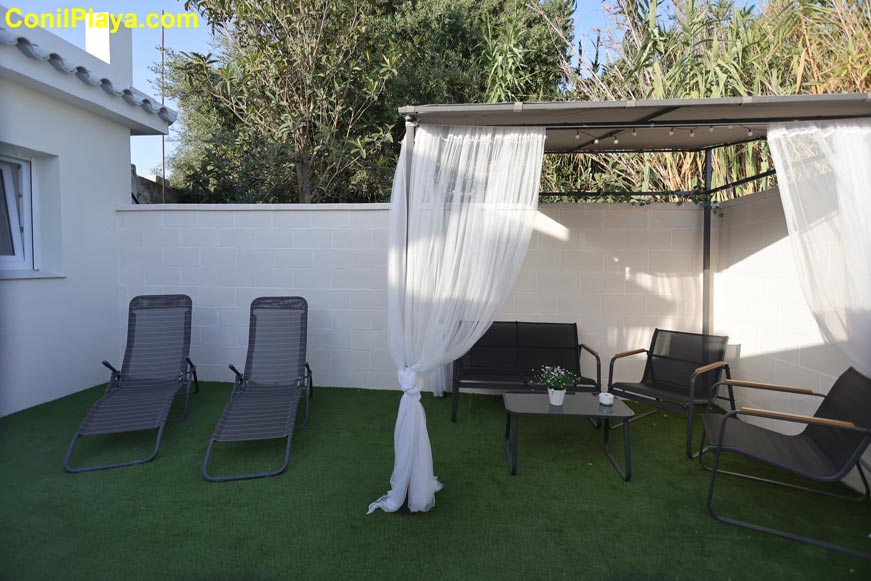 Zona de jardín con tumbonas y pérgola con cortinas junto a una vivienda