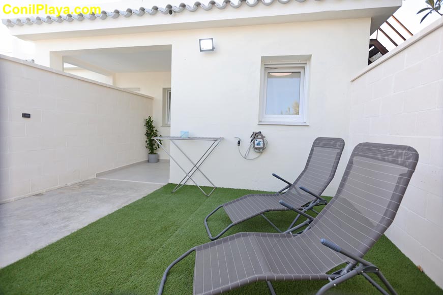 Zona exterior de la casa con césped artificial y dos tumbonas visibles