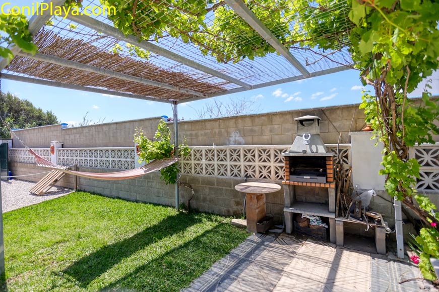 Jardín con barbacoa y hamaca y estructura metálica con una parra