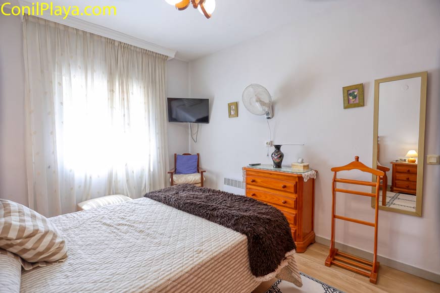 Dormitorio con televisión, cama doble y muebles de madera vistos desde la entrada