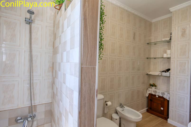Baño con ducha de azulejos, bidé y estantería con toallas visibles
