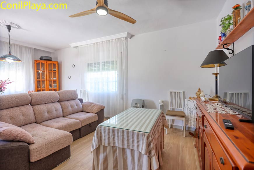 Salón con sofá grande mesa central, ventilador de techo y mueble de televisión de madera
