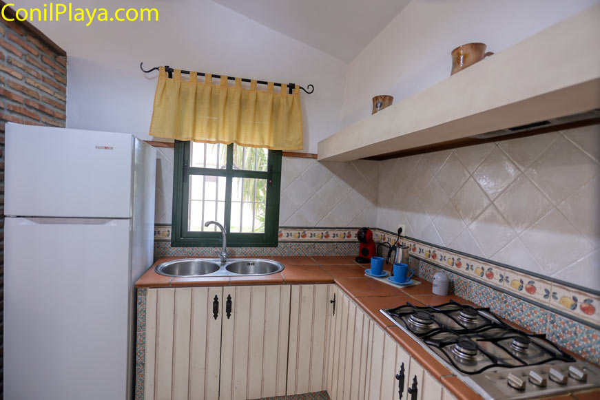 Cocina con hornilla a gas, fregadero bajo la ventana y frigorífico