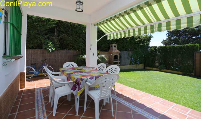 porche con toldo, mesa y sillas. Al fondo la barbacoa