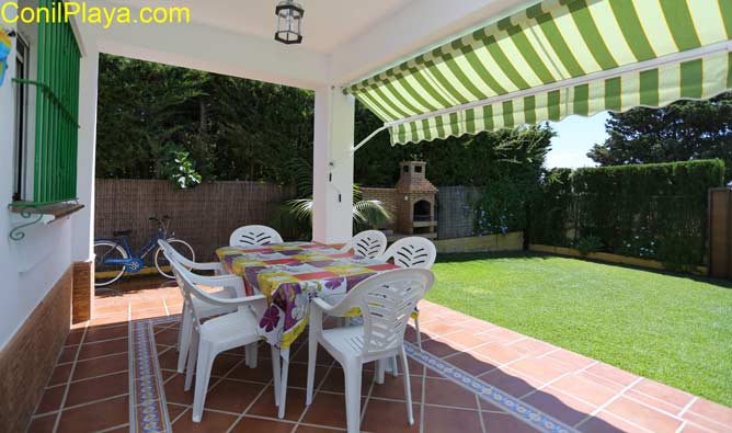 porche con toldo, mesa y sillas. Al fondo la barbacoa