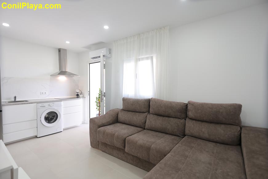 Salón con sofa chaise longue y cocina integrada moderna blanca