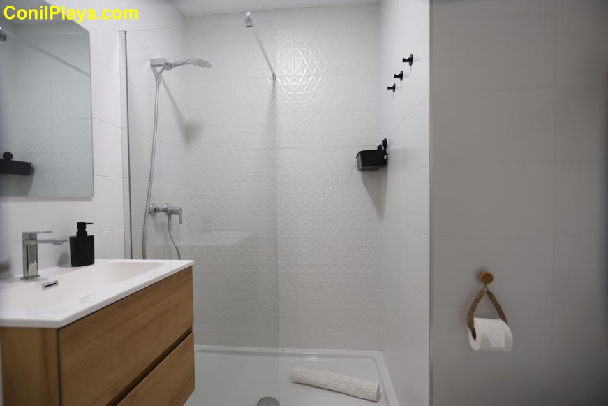 Cuarto de baño moderno con ducha y lavabo con cajones color madera visto desde la entrada