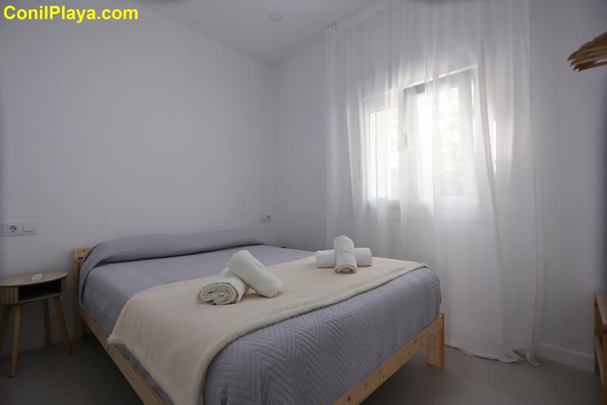 Perspectiva general del dormitorio principal con cama doble, ventana grande y decoración sencilla