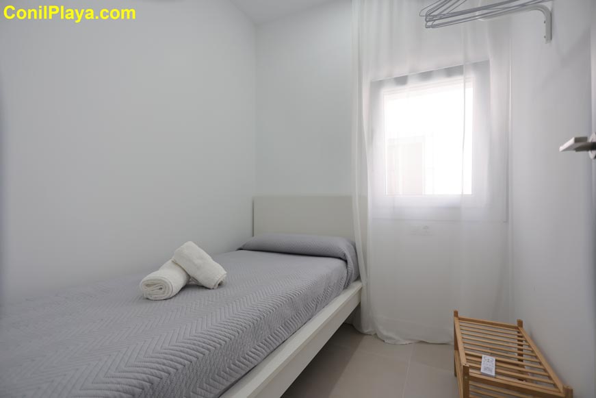 Dormitorio secundario sencillo con cama individual y ventana con cortinas blancas
