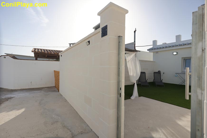 Entrada de patio privado con césped artificial y tumbonas junto a la casa