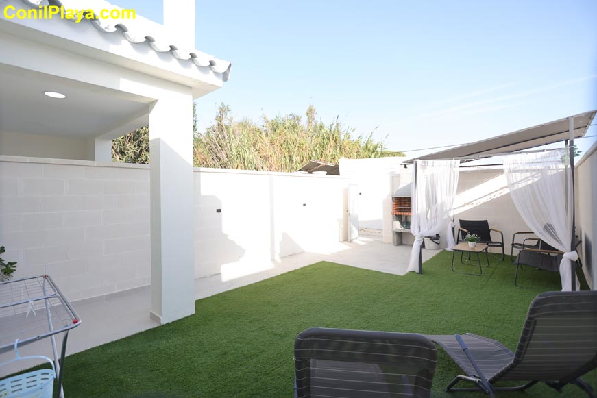 Jardín privado con césped artificial, zona de estar y pérgola con cortinas
