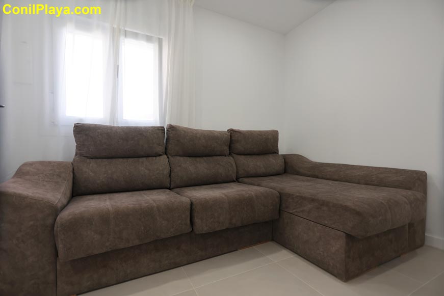 Vista frontal del sofá chaise longue junto a ventana con cortinas blancas