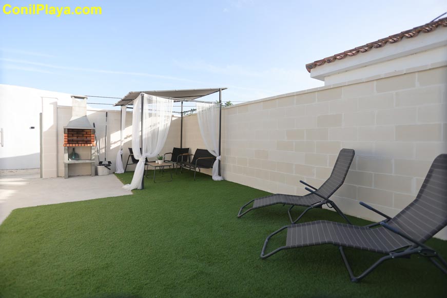 Zona ajardinada con tumbonas, barbacoa y área de sombra bajo la pérgola