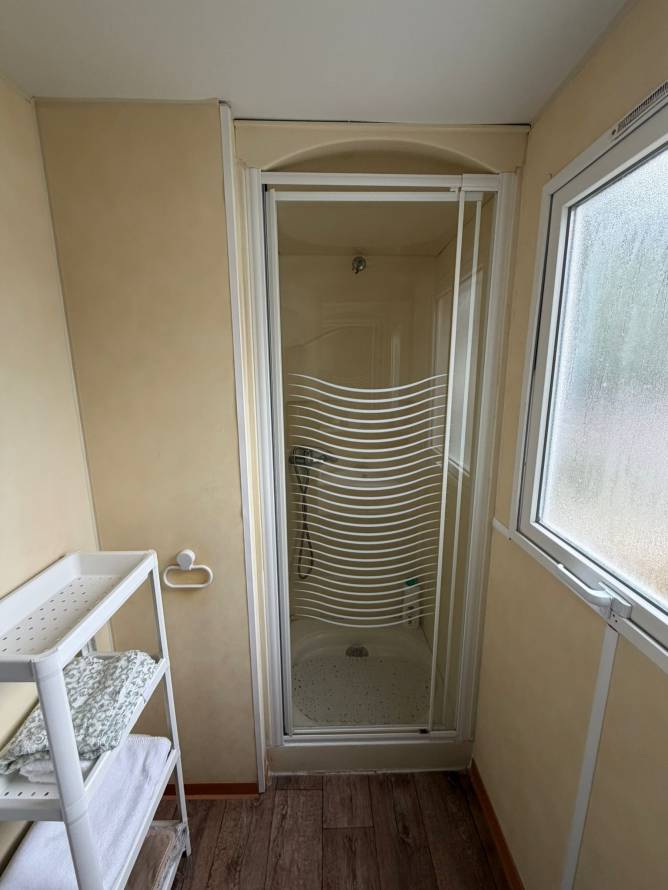 Cuarto de baño con ducha cerrada, ventana y estantería con toallas