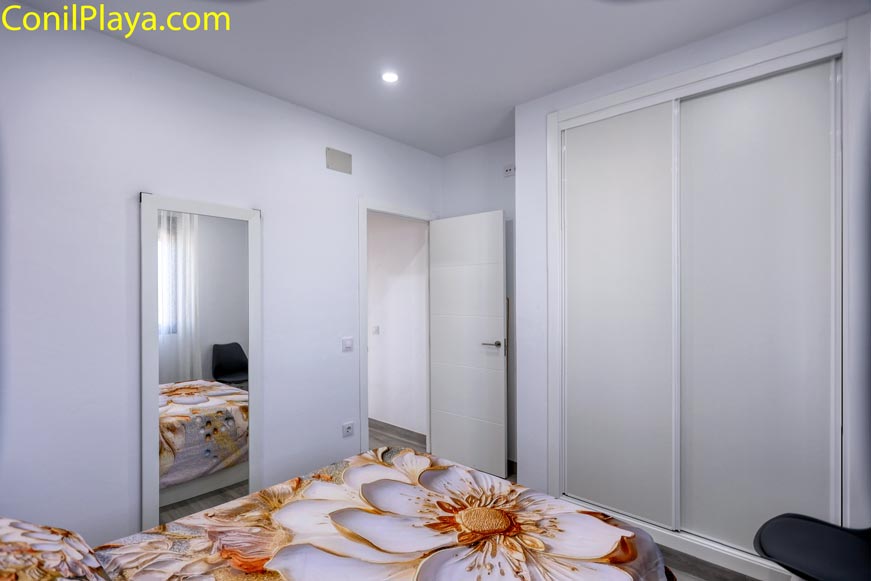 Dormitorio con armario empotrado, espejo y cama con colcha floral