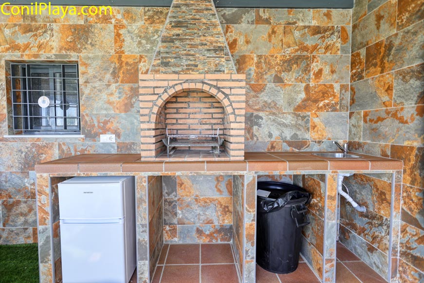 Zona de barbacoa con frigorífico y fregadero bajo porche de vivienda