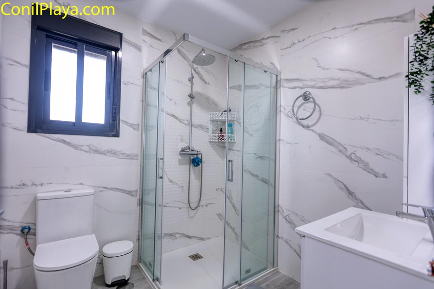 Cuarto de baño moderno con ducha mampara y ventana desde la entrada