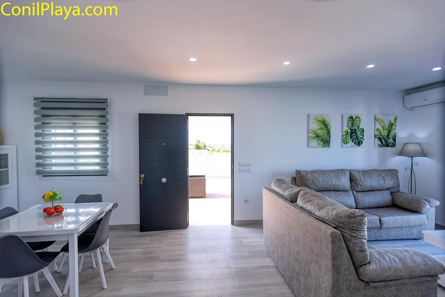 Salón con sofá gris y mesa de comedor junto a puerta de entrada