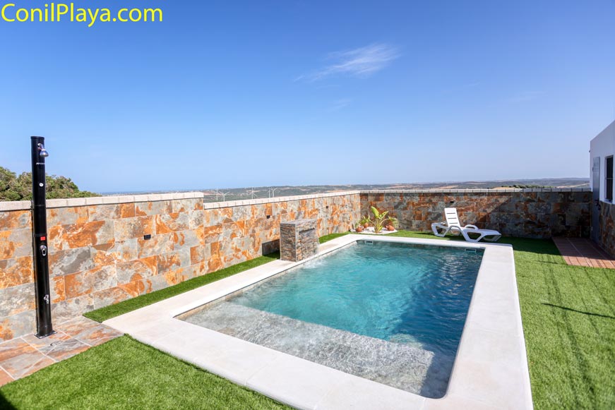 Piscina privada junto a muro de piedra vista desde zona de césped artificial
