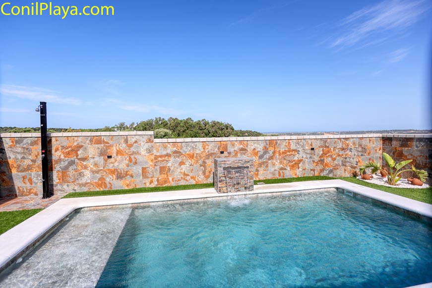 Piscina privada con ducha exterior y muro de piedra vista desde el borde