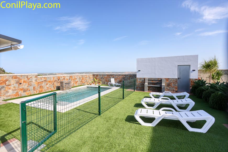 Zona exterior con piscina vallada, césped artificial y varias tumbonas blancas