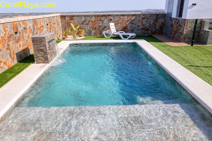 Piscina privada junto a vivienda con dos tumbonas y cascada