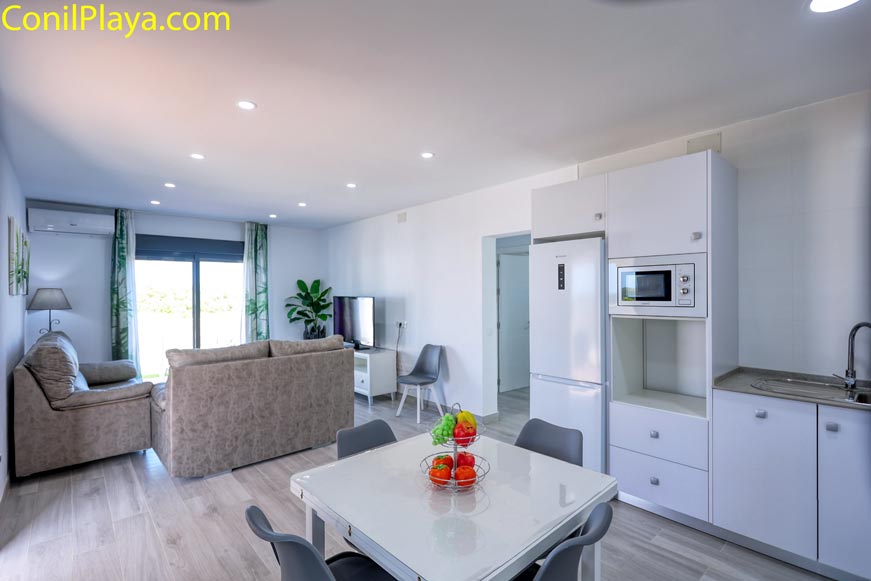 Salón moderno con cocina abierta, mesa y dos sofás vistos desde la entrada