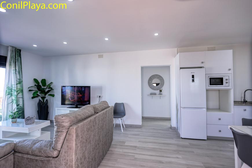 Salón moderno con sofá gris y cocina abierta al fondo iluminada