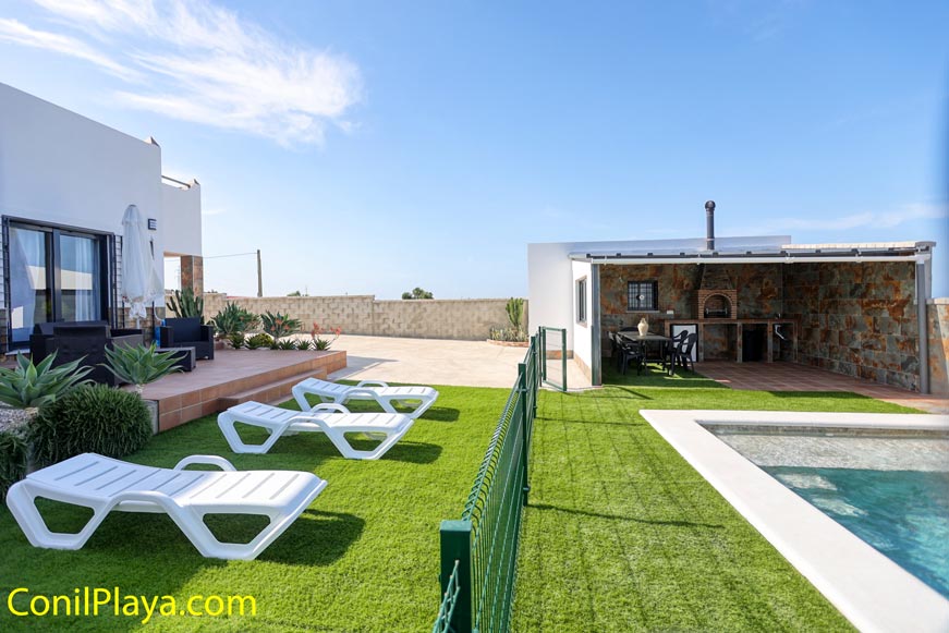 Zona exterior con piscina tumbonas césped artificial y barbacoa techada visible