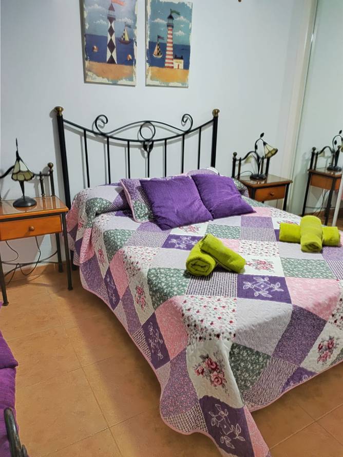 Dormitorio principal con cama doble, cojines morados y cuadros decorativos