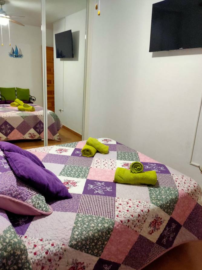 Dormitorio con cama grande colcha colorida y televisión en la pared