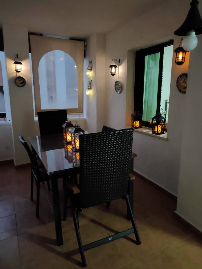 Terraza iluminada de noche con mesa y faroles vista desde una esquina