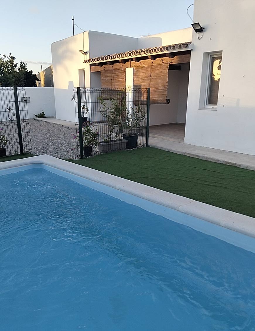 Piscina exterior junto a césped artificial, terraza cubierta y fachada blanca moderna