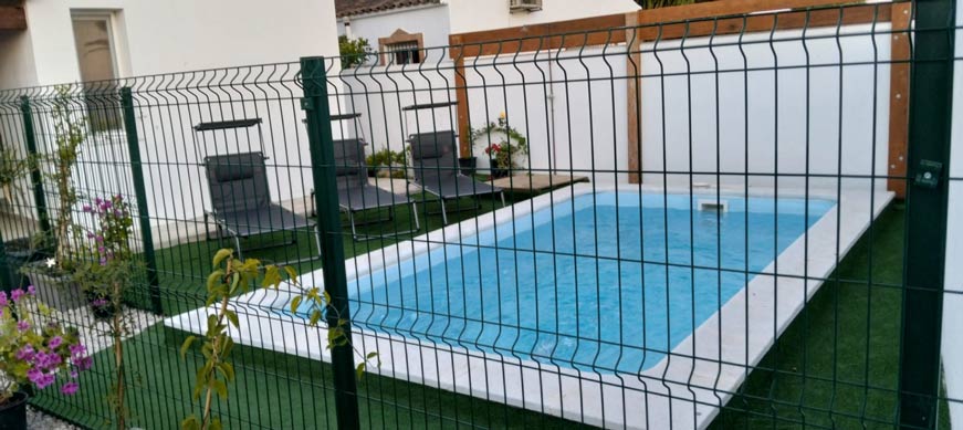 Piscina pequeña privada al aire libre, rodeada de césped artificial y tumbonas junto a una valla metálica.