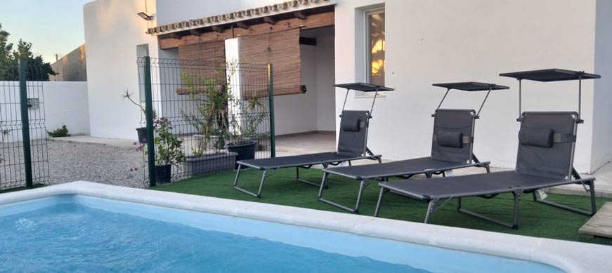 Piscina pequeña al aire libre junto a tumbonas grises, césped artificial y fachada blanca moderna